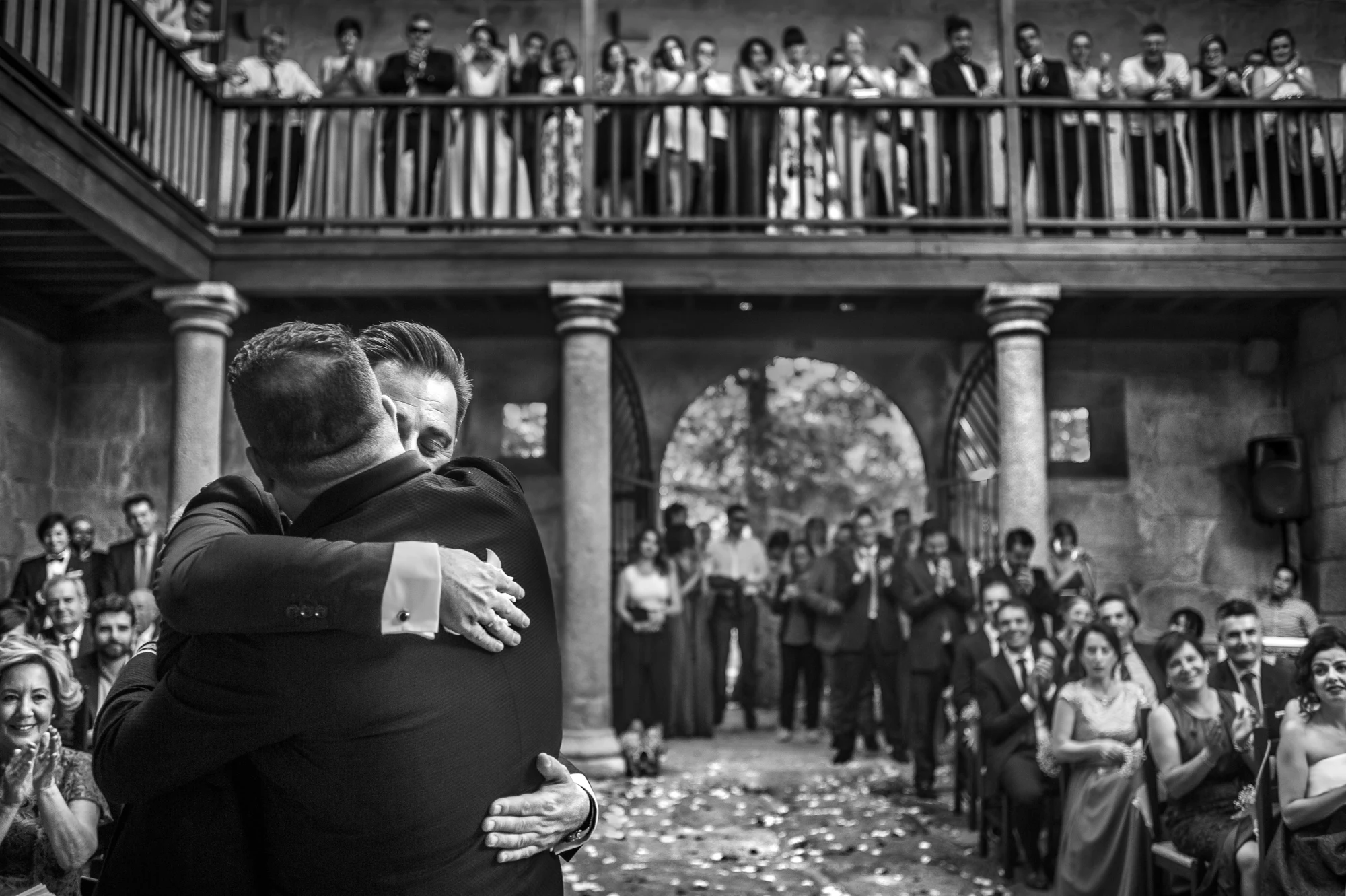 Black and white embrace in a courtyard as guests watch from balconies