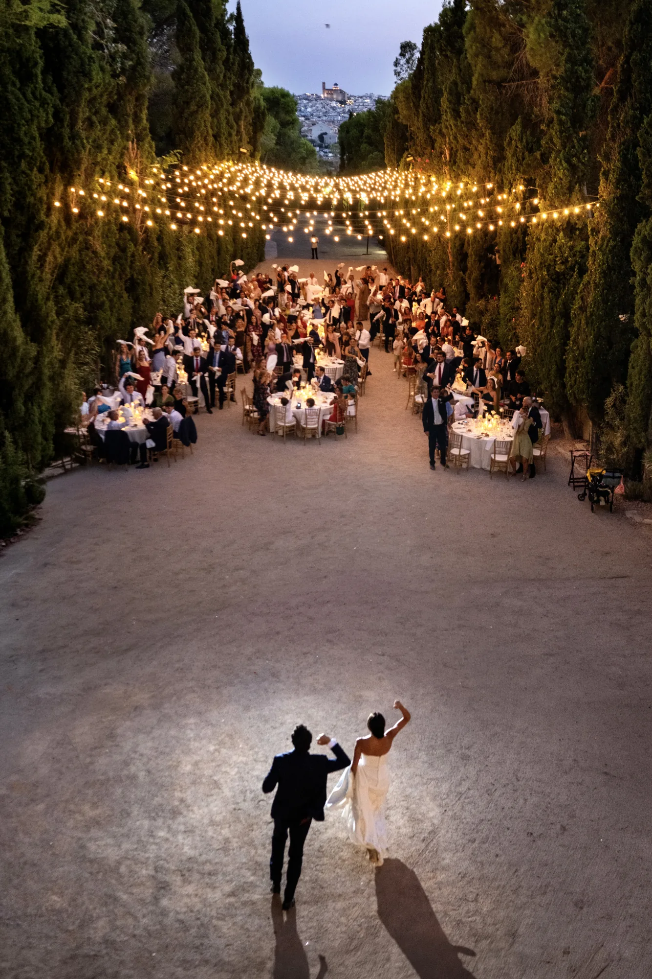 Couple walking towards a candlelit garden reception under strings of lights